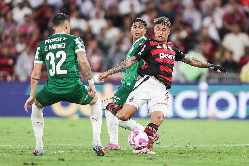Jogador do Flamengo se prepara para chutar cercado por jogadores do Palmeiras.