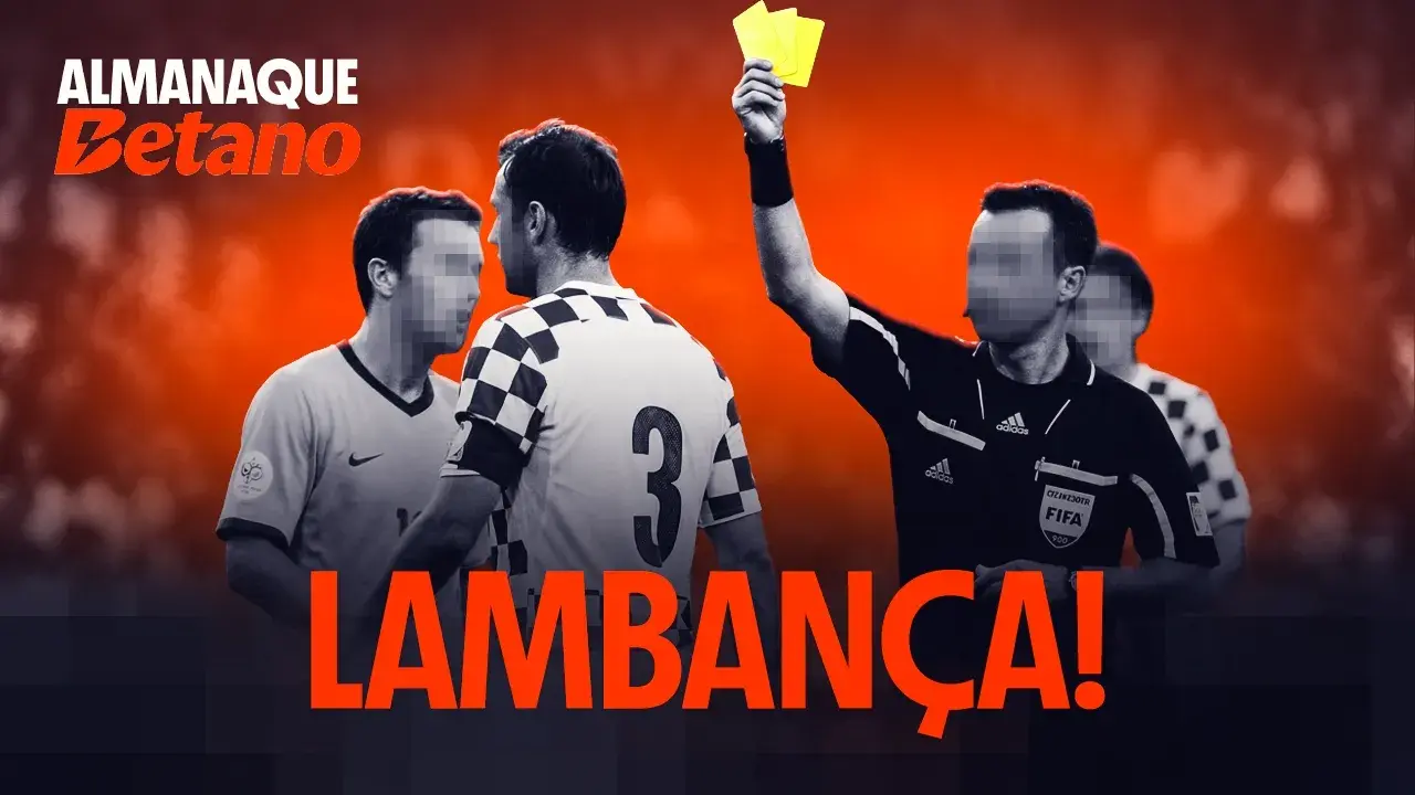 Em primeiro plano, um árbitro de futebol levanta um cartão amarelo. Atrás dele, dois jogadores discutem cara a cara.